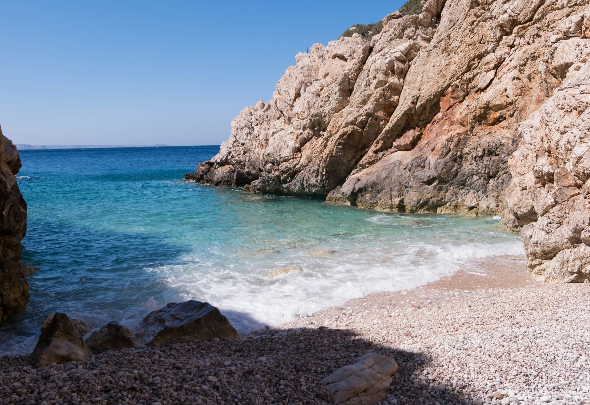 A small pebble cove between pale cliffs and clear blue sea